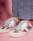 model wearing light wash denim jeans  and silver leather sneaker sneakers in front of pink background