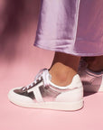 model wearing lilac satin skirt and silver leather sneaker sneakers in front of pink background