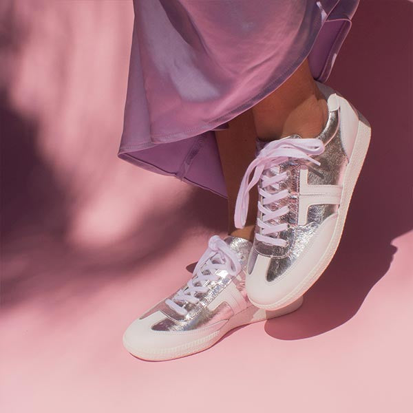 model wearing lilac satin skirt and silver leather sneaker sneakers in front of pink background