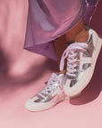 model wearing lilac satin skirt and silver leather sneaker sneakers in front of pink background