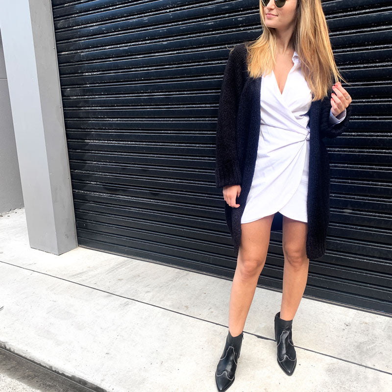 model in white dress, black cardigan and Black leather, western heeled Billi Bi ankle boots with silver stud detail