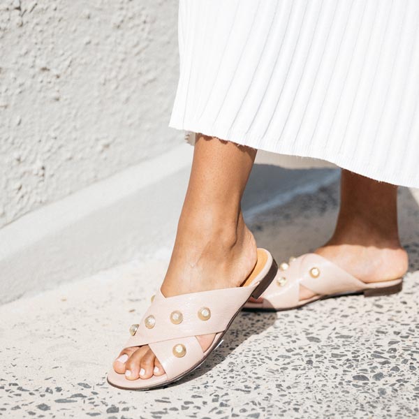 close up of light pink textured leather Billi Bi flat crossover slide with gold stud detail on model's feet