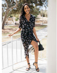 Low heel studded leather sandal worn by model wearing floral dress with black handbag