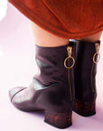 Mint&Rose sol carey black ankle boot with low acrylic heel on model facing backwards in orange dress