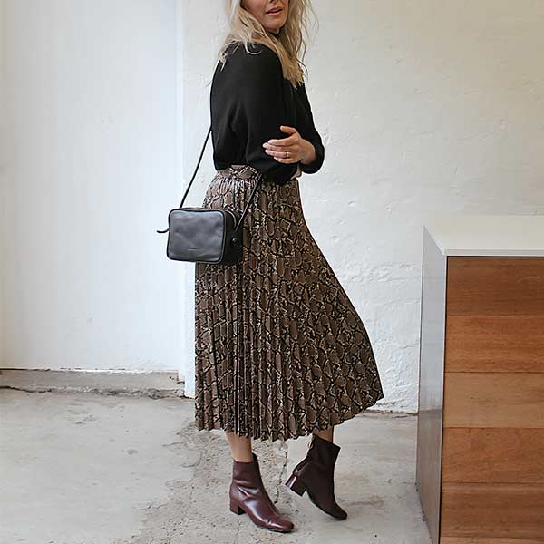 model wearing black knit, snakeprint pleated skirt, black crossbody bag and Mint&Rose sol wine leather ankle boot 